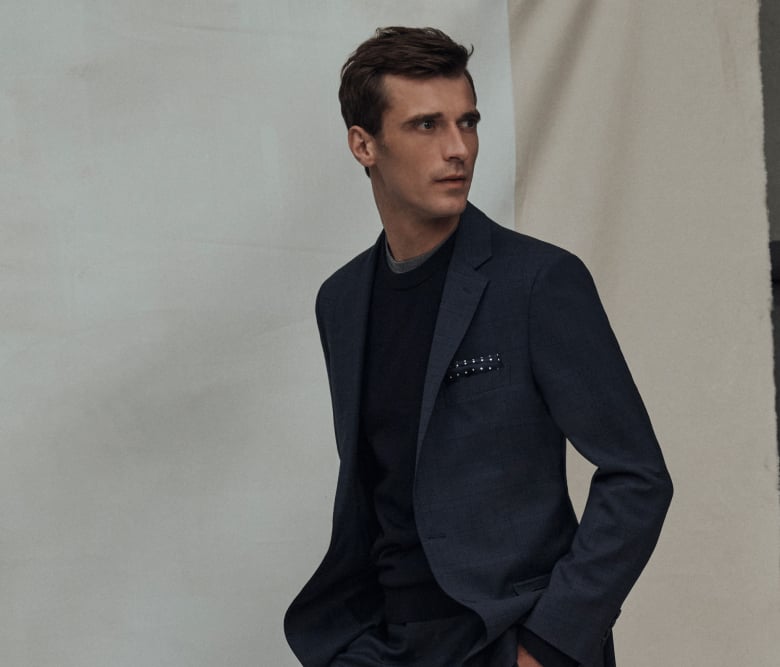 Ein Mann in einem eleganten dunkelblauen Blazer, kombiniert mit einem schicken Pullover, einem bequemen T-Shirt und einem ordentlich gefalteten Einstecktuch