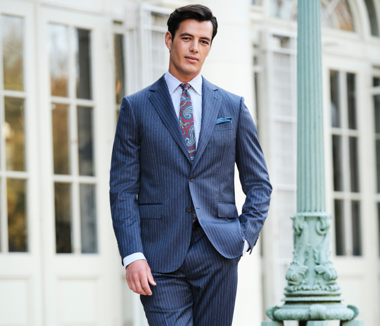 Un hombre con traje gris oscuro, camisa azul y corbata, de pie y con actitud profesional